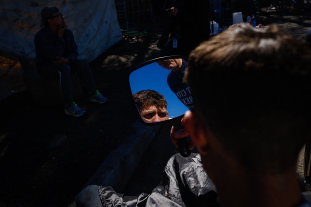 Scott Llewellyn mira su nuevo corte de pelo mientras Joseph Kautz sostiene un espejo en un campamento en Redwood City, California, el sábado 10 de febrero de 2024. (Shae Hammond/Bay Area News Group)