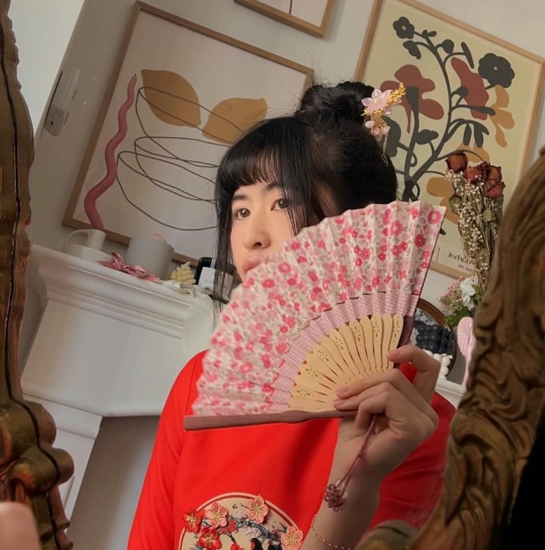 Una mujer con un hermoso peinado mira a la cámara desde detrás de un abanico con un diseño floral.