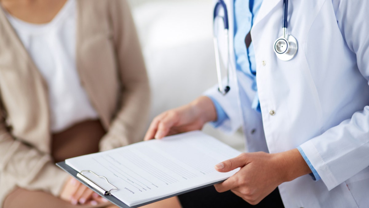 Una doctora sosteniendo un formulario de receta mientras habla con un paciente