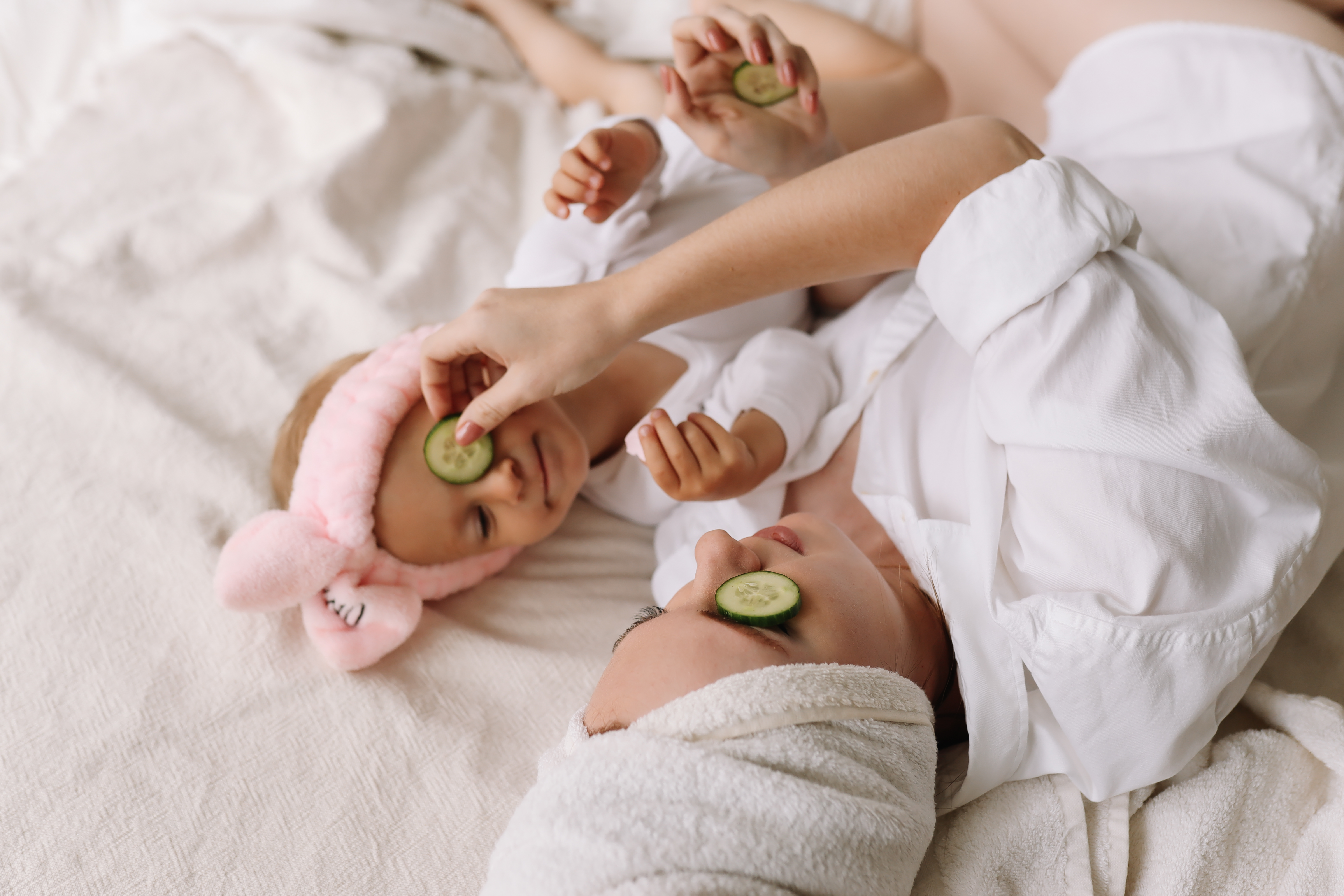 Madre e hijo descansando en una cama con rodajas de pepino sobre los ojos, el niño sosteniendo una piedra de flor rosa.