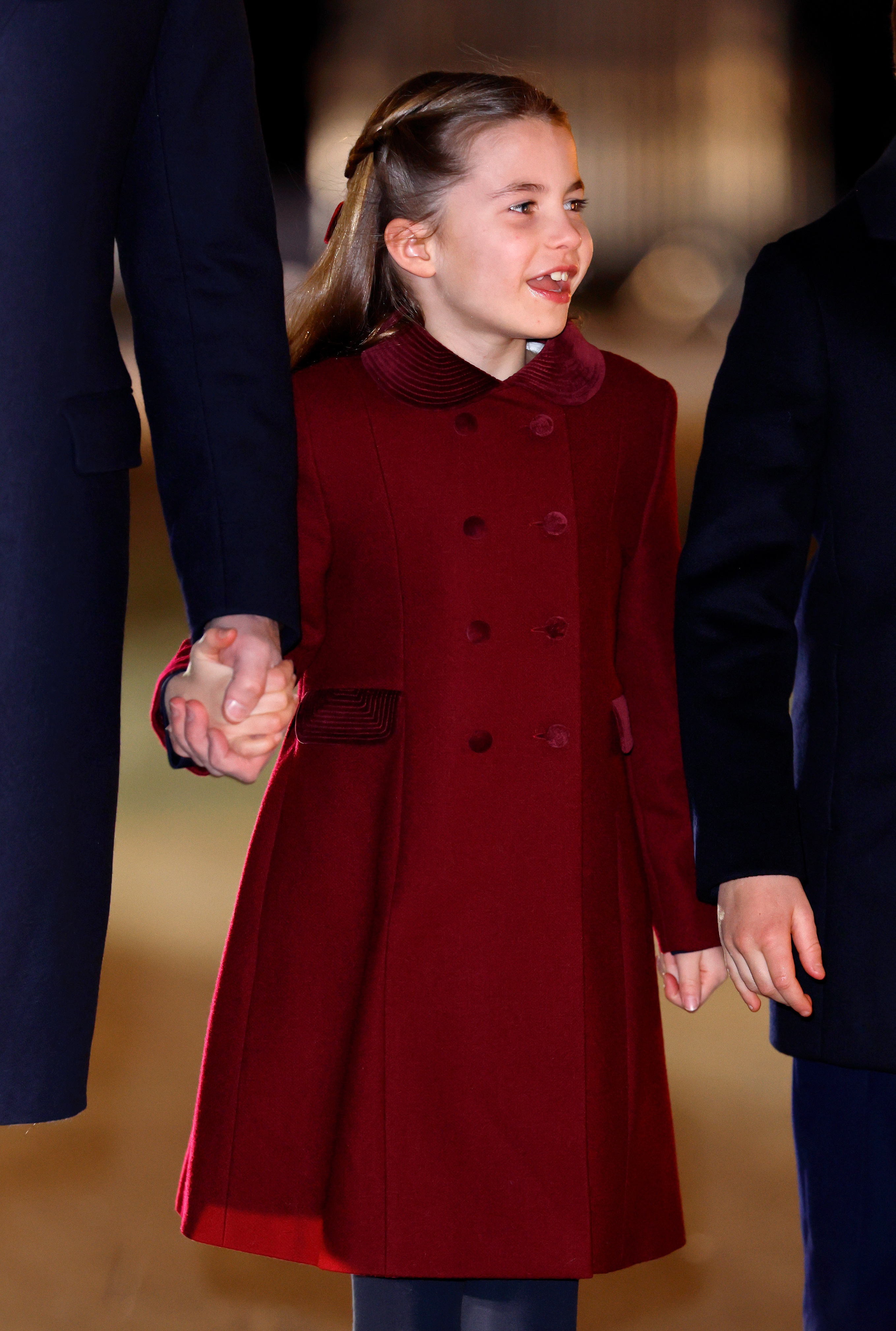 La princesa Charlotte viste un abrigo color burdeos y sonríe mientras toma la mano del príncipe William.
