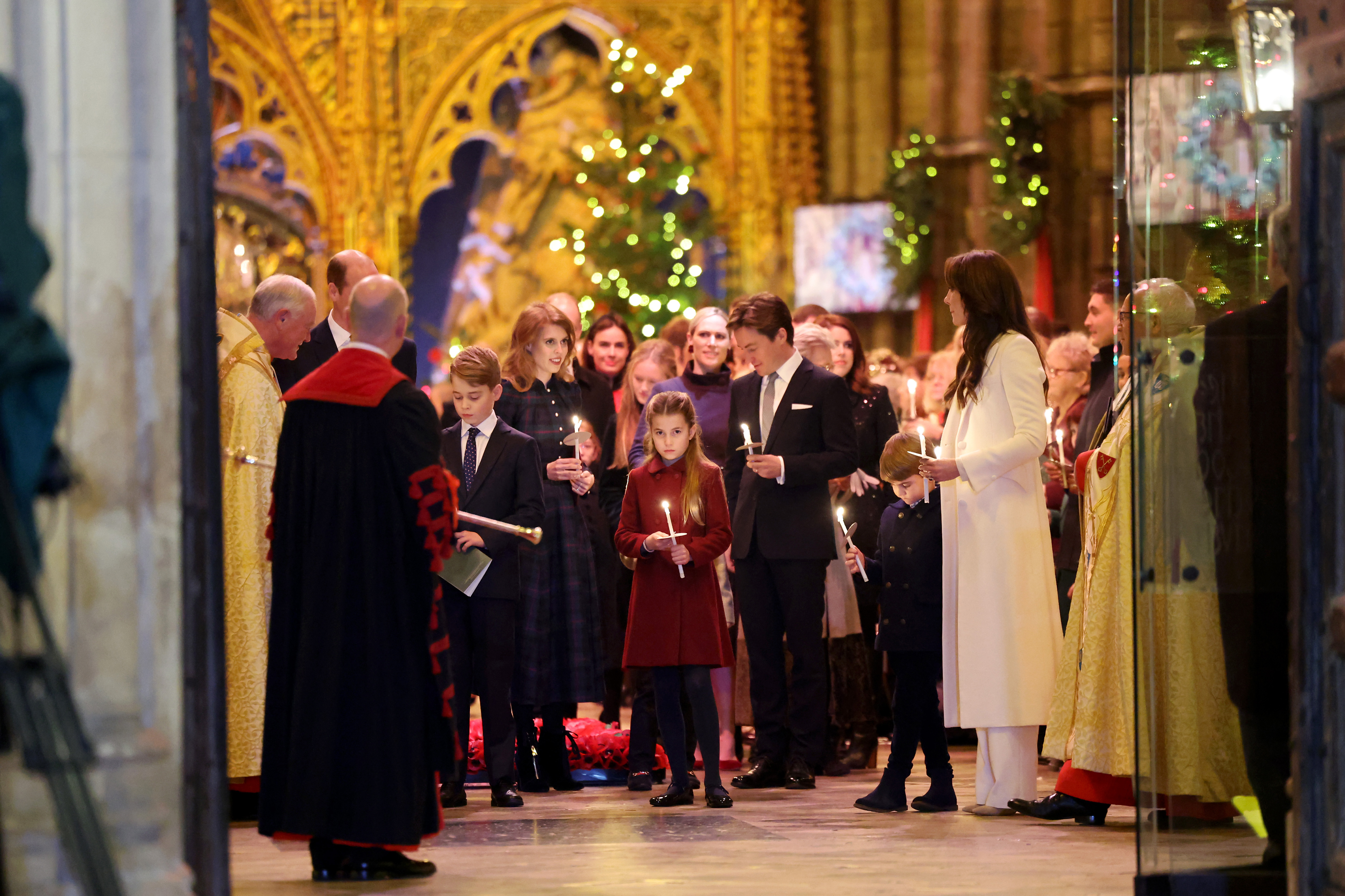 La princesa Charlotte junto a la princesa Kate, el príncipe Louis, el príncipe George, la princesa Bearrice y otros miembros de la familia real en la Abadía de Westminster sosteniendo una vela.