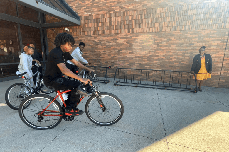 El estudiante de tercer año, Elyazar Holiday, dice que su bicicleta le ayuda a tomar los autobuses que necesita para llegar a Davis Aerospace High School. Aquí, aparece fotografiado con sus amigos montando en bicicleta frente a la escuela.